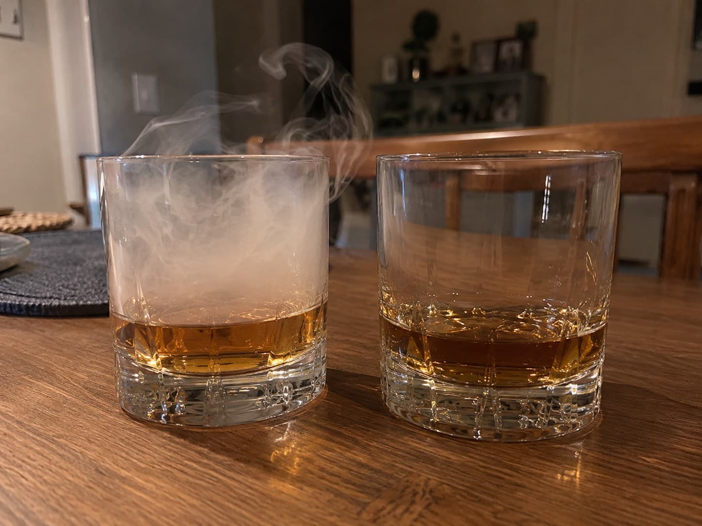 Two tumblers of the same whisky side by side, one filled with smoke and one plain